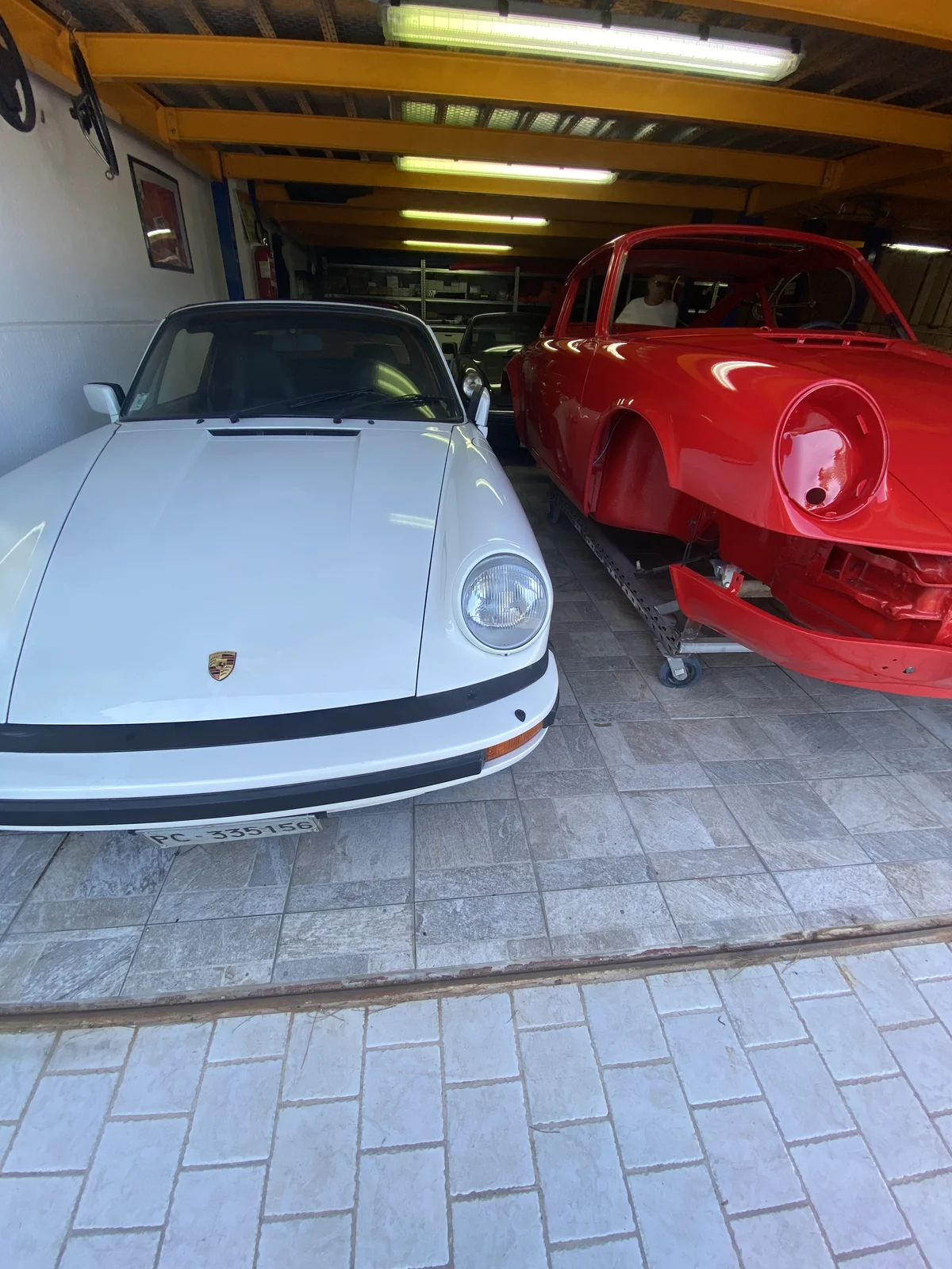 Completed white Porsche 911 alongside a bare red shell in the workshop